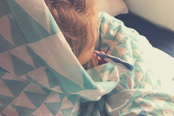 child snuggled in bed with a thermometer 