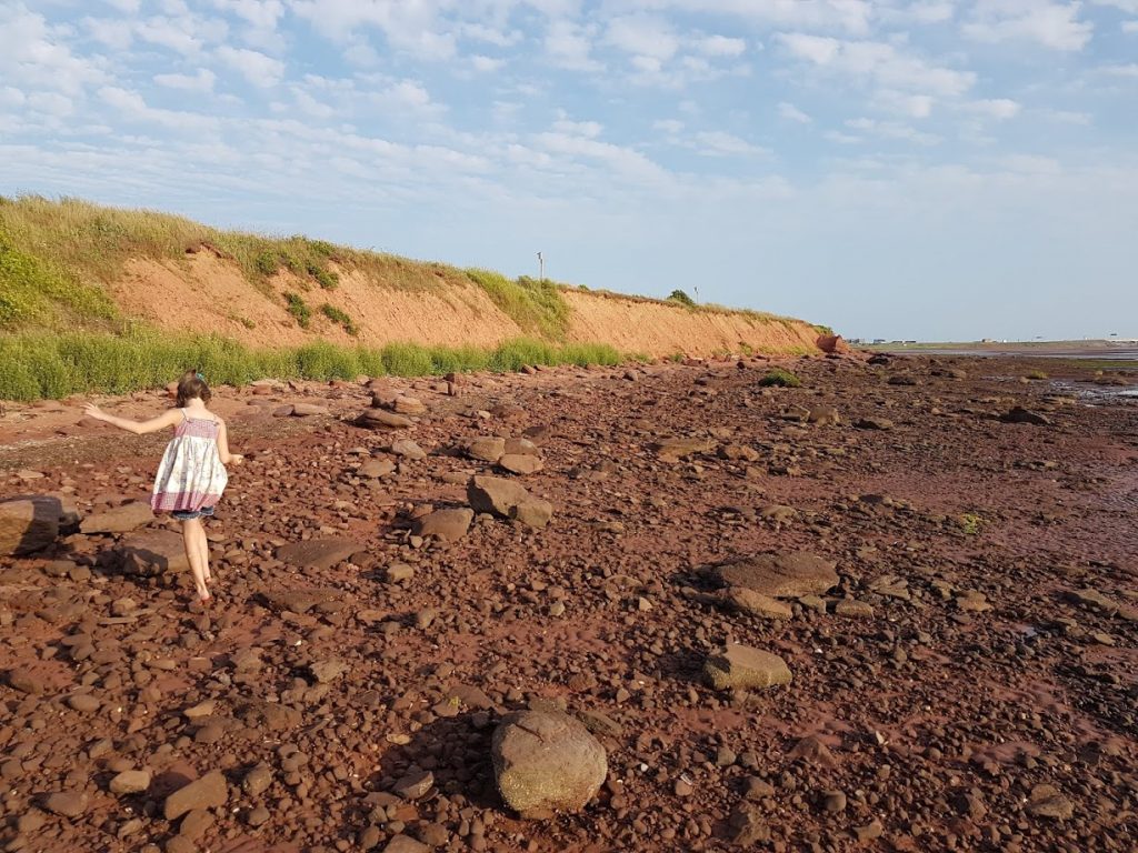 girl walking along red sand of prince edward island - plan your pei vacation