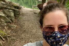 masked woman wearing sunglasses in front of picnic table and pond