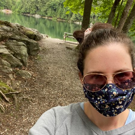 masked woman wearing sunglasses in front of picnic table and pond